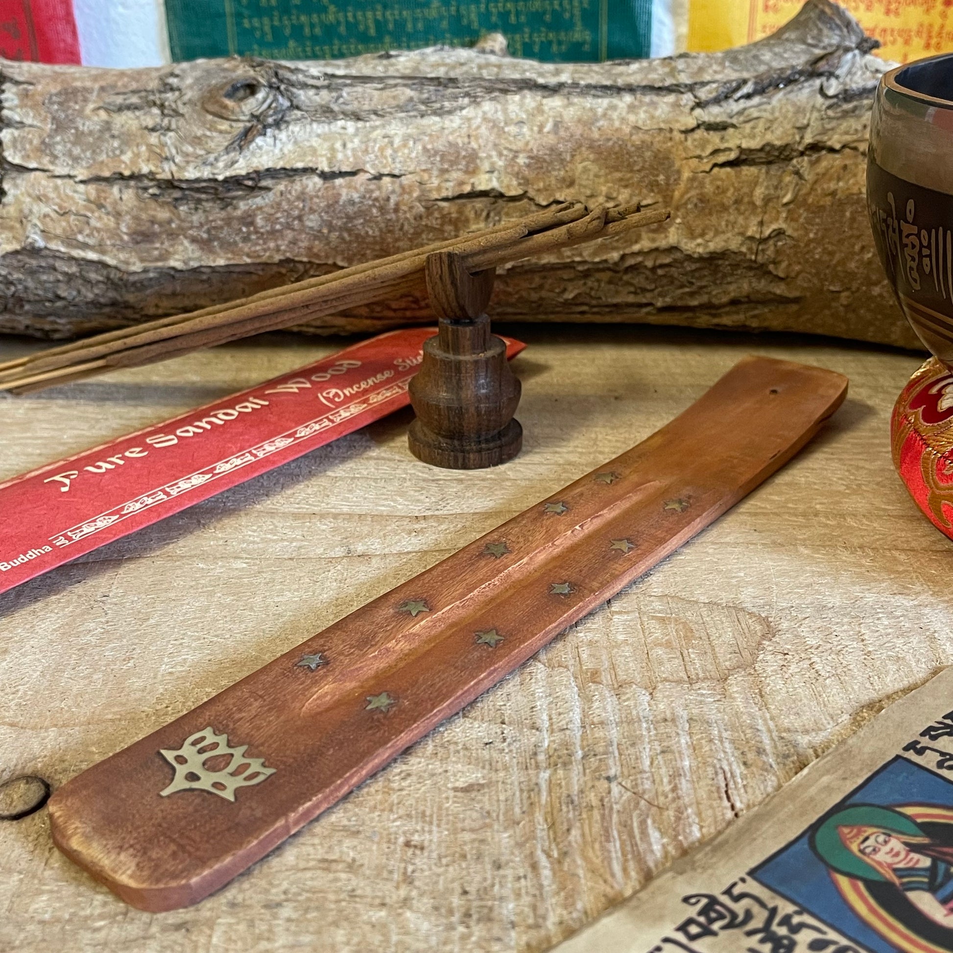 This best-selling incense holder features a unique shoehorn shape, crafted from durable mango wood and designed as an effective ash catcher. Inlaid with brass stars and a lotus flower, this piece adds a touch of elegance and spirituality to any space. The long, slightly curved design holds incense sticks securely, allowing ash to collect neatly along the wooden body for easy cleanup.