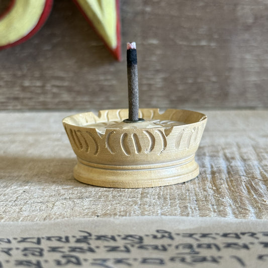 Wooden incense burner with a single stick of incense on a textured surface.