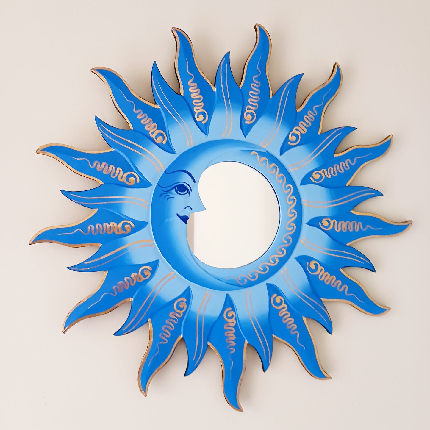 Elevate your home with the mystical charm of our Sun &amp; Moon Mirror. Lovingly handmade by fairtrade artisans, this unique piece features a beautifully painted sun and moon design in vibrant blue tones. Perfect for adding a touch of spirituality, harmony, and positive energy to your living space, this mirror doubles as both a functional piece and captivating art. Ideal for bedrooms, meditation spaces, or as a thoughtful gift for someone special.
