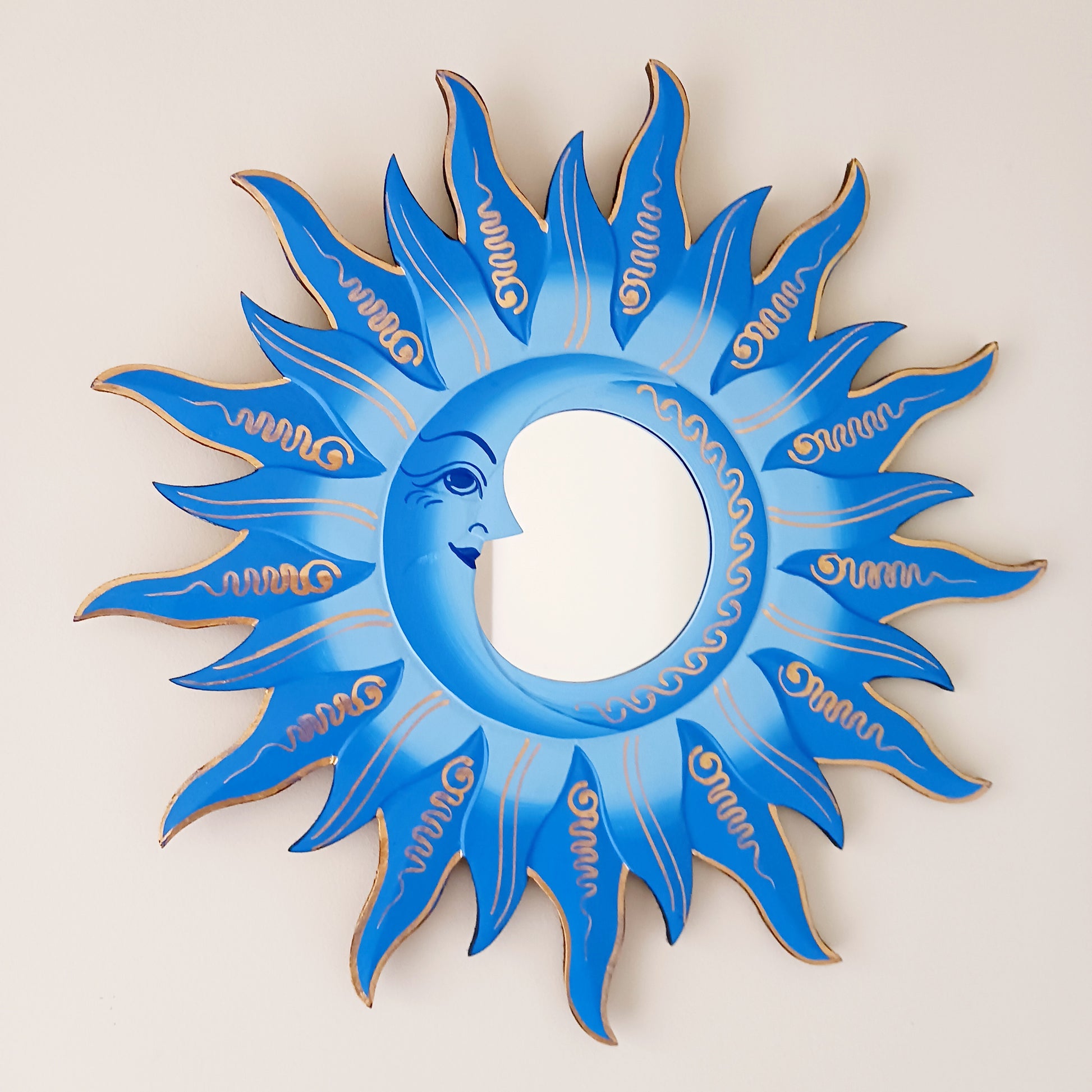 Elevate your home with the mystical charm of our Sun &amp; Moon Mirror. Lovingly handmade by fairtrade artisans, this unique piece features a beautifully painted sun and moon design in vibrant blue tones. Perfect for adding a touch of spirituality, harmony, and positive energy to your living space, this mirror doubles as both a functional piece and captivating art. Ideal for bedrooms, meditation spaces, or as a thoughtful gift for someone special.