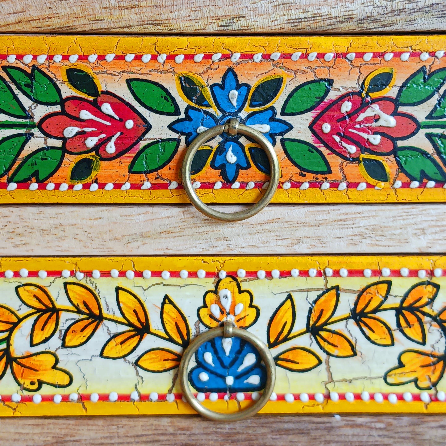 Add charm and functionality to your space with the Zaha Hand-Painted 6 Drawer Mango Wood Chest. Standing gracefully on low corner feet, this artisan-crafted piece features a vibrant blend of hand-painted leafy vines, amber-toned framing, and highlighted beading. Each drawer is uniquely designed and fitted with elegant gold-toned ring pull handles, offering a burst of colour and creativity.