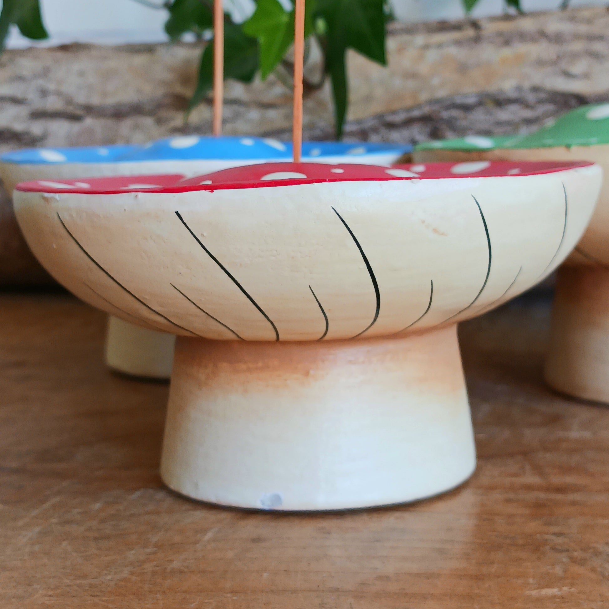 Bring woodland charm to your space with these hand-painted wooden mushroom incense holders. Each piece features a white stalk and a vibrant, spotty cap in your choice of blue, green or red. Designed with a central incense stick holder, these mushrooms are perfect for adding a whimsical, on-trend touch to your décor.