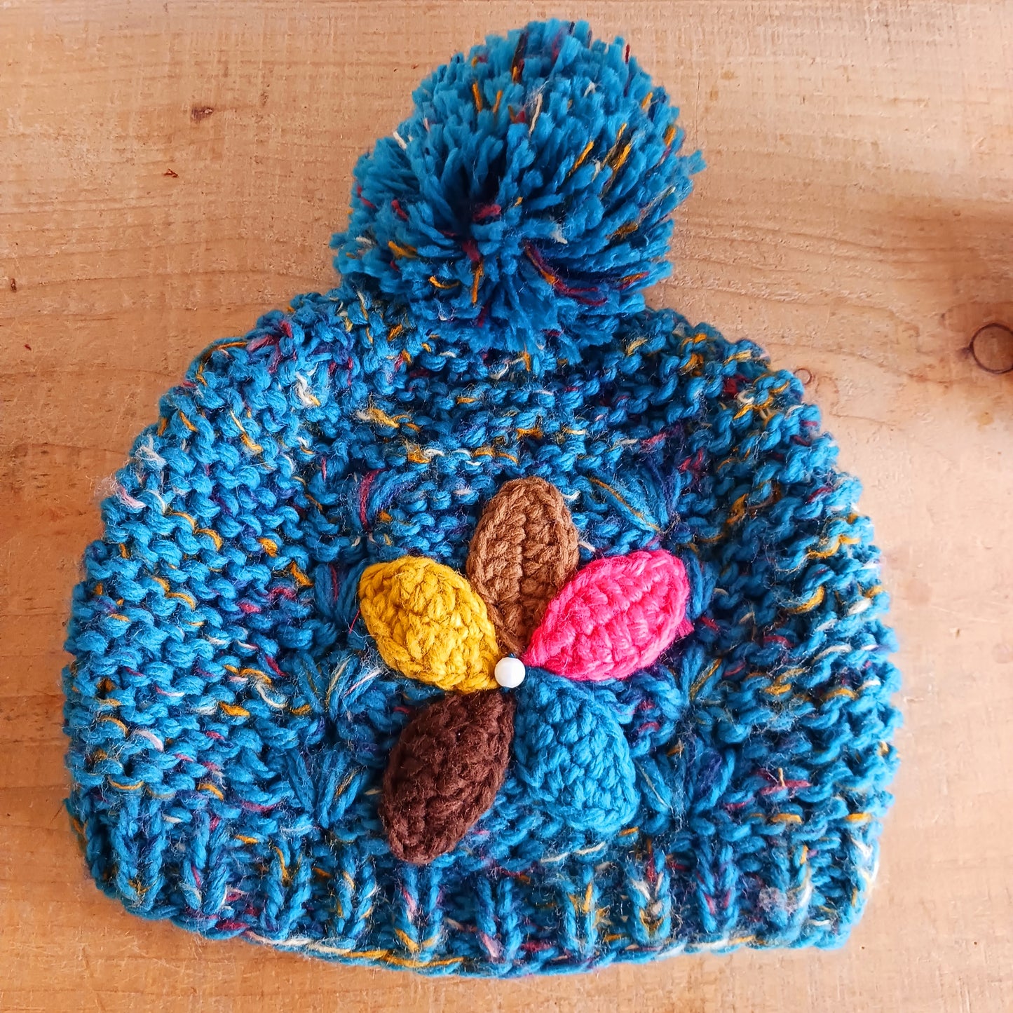 Stay warm in style with this charming knitted wool flower bobble hat, designed to bring both comfort and personality to your winter wardrobe. Crafted from soft, insulating wool, this cozy beanie keeps you snug even on the coldest days.