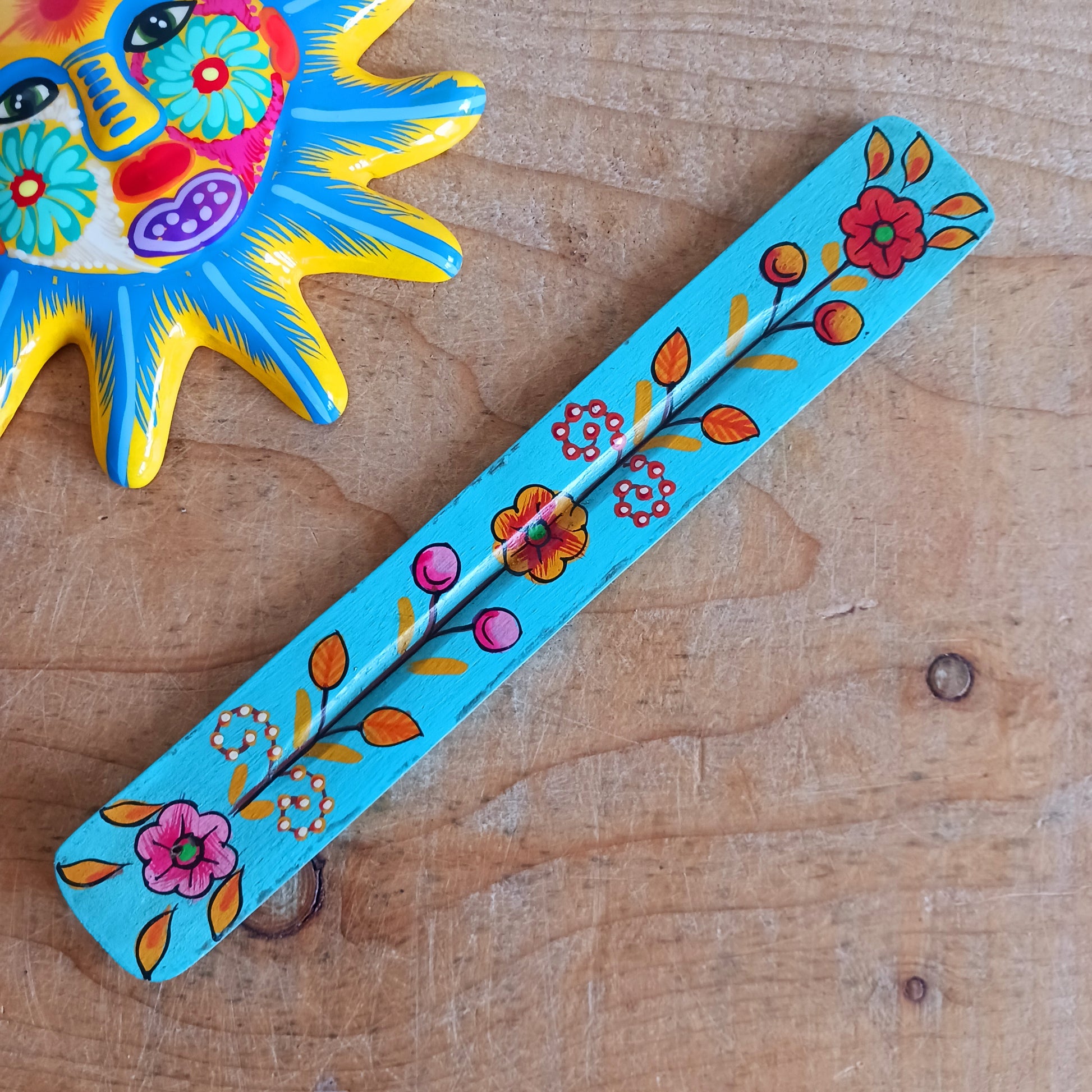 This wooden incense stick holder is hand-painted with decorative floral designs. Sourced from India in a fairtrade manner, this product serves as both an aesthetically pleasing decoration and an effective ash catcher for any home.