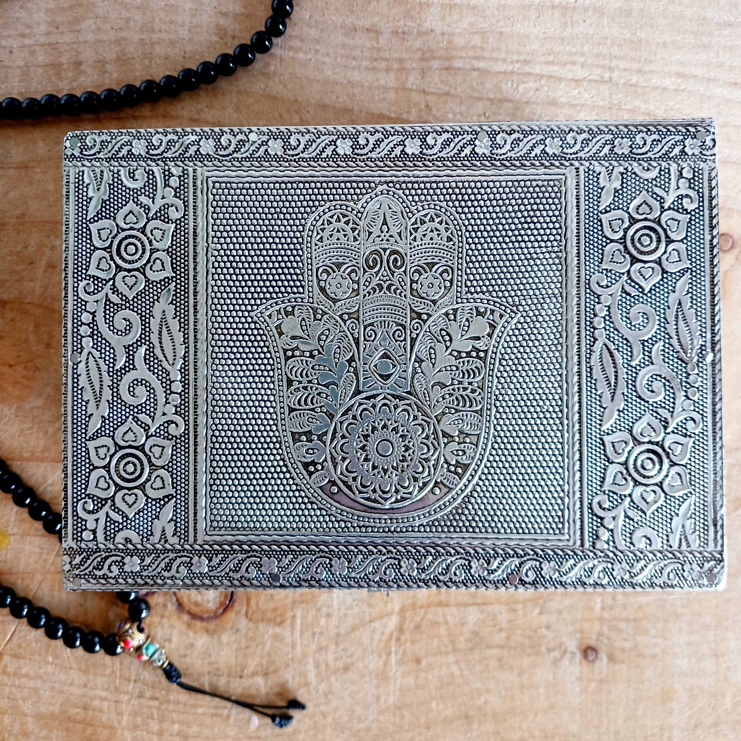 This beautiful silver colour embossed aluminium jewellery box has plenty of space for you to keep you jewellery and other valueables, and comes with a pull-out drawer.  It is lined with black cotton velvet and intricately decorated with a hamsa hand on the lid, and ornate bordering.