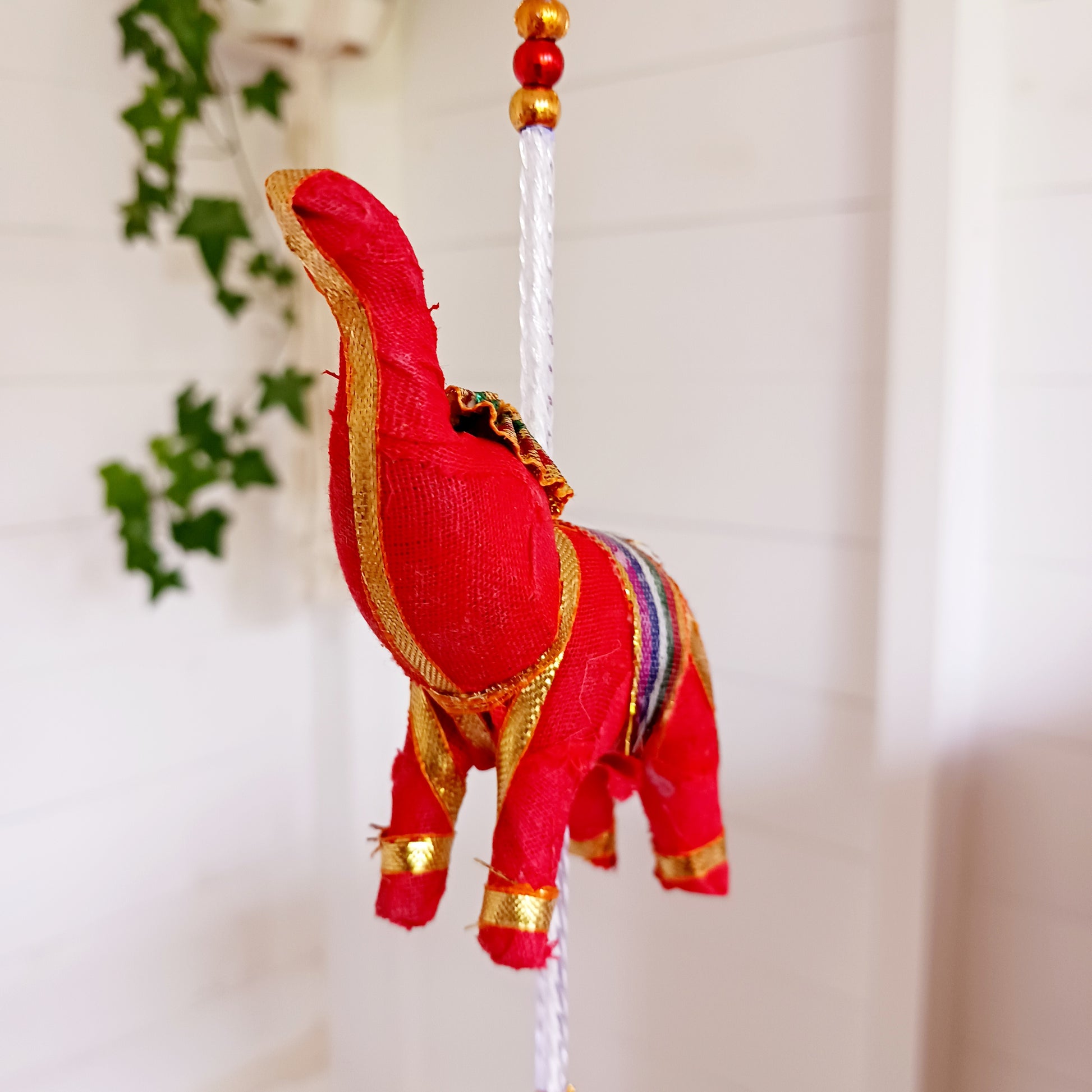 Bring vibrant charm and a touch of global-inspired décor into your home with this beautifully handcrafted stuffed elephant hanging garland. Designed in a traditional tota bell style, this decorative piece features a string of brightly coloured fabric elephants, carefully interspersed with playful beads, mini pom-poms, and delicate jingly bells.