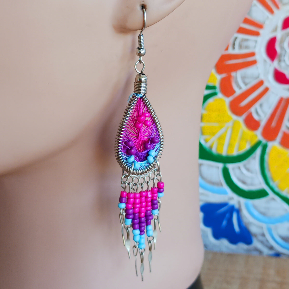 Add a splash of colour to your look with these beautiful handmade Peruvian woven teardrop earrings. Inspired by the vibrant colours and patterns of a peacock feather, each earring features intricate woven detailing complemented by coordinating beads and delicate silver-tone embellishments.