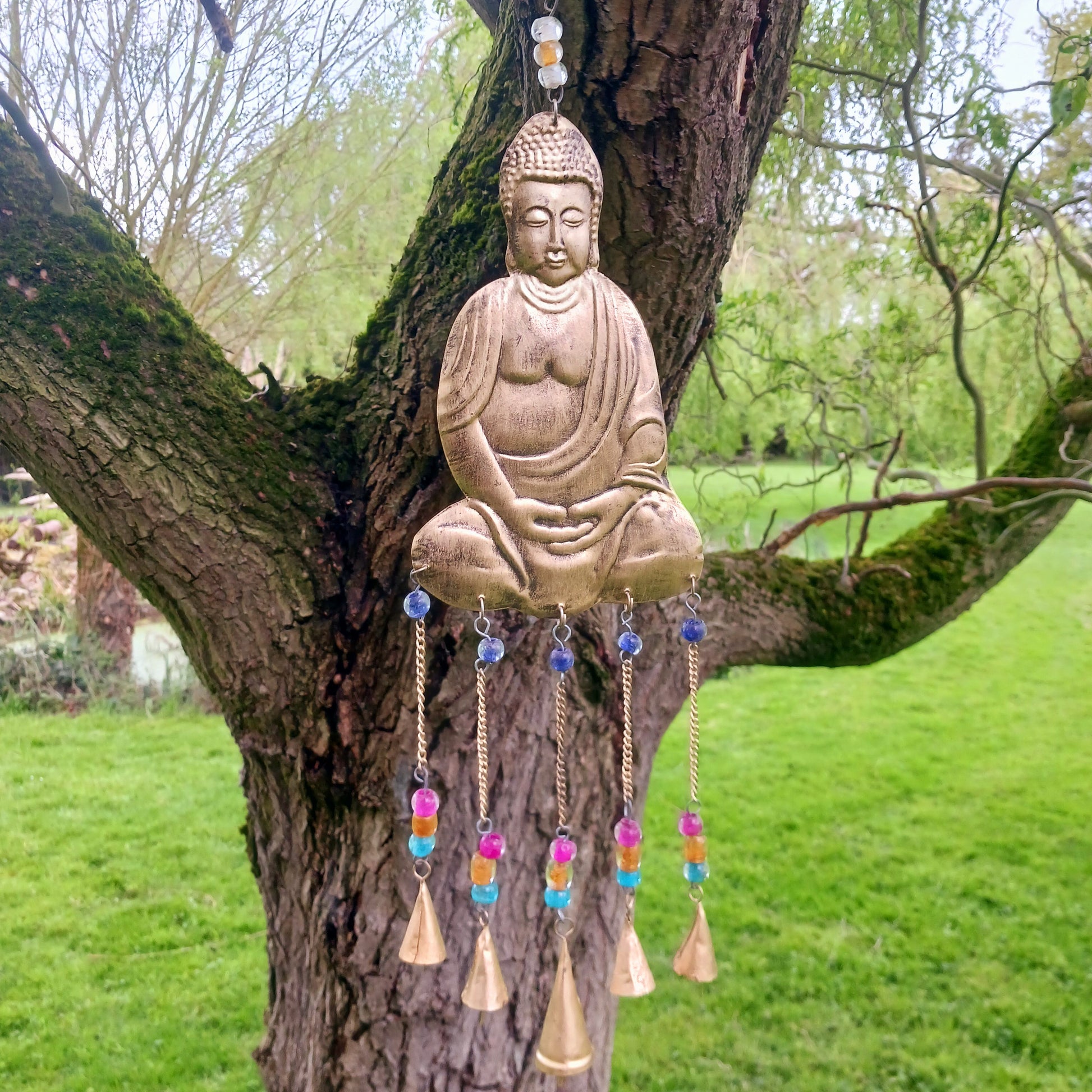 This lovely Buddha 5 bell windchime will bring serenity and cultural charm to any space.  Made in India from brass, this chime features a beautifully detailed Buddha adorned with colourful beads. 
 The five brass bells create a calming melody with every breeze, making it a perfect addition to meditation spaces, gardens, or tranquil home settings.