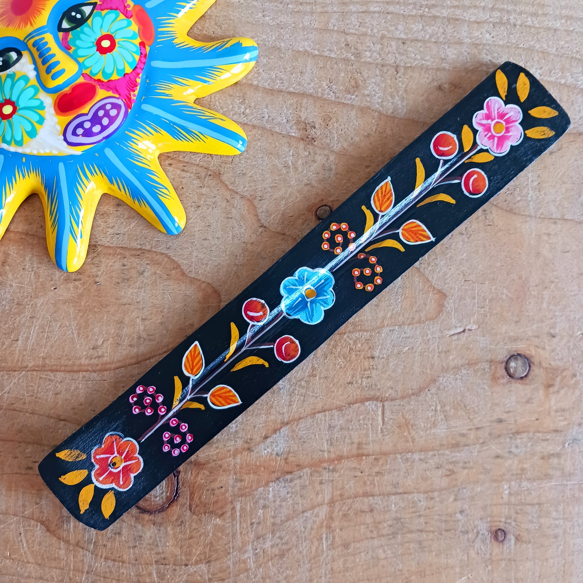 This wooden incense stick holder is hand-painted with decorative floral designs. Sourced from India in a fairtrade manner, this product serves as both an aesthetically pleasing decoration and an effective ash catcher for any home.