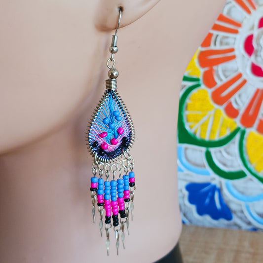 Add a splash of colour to your look with these beautiful handmade Peruvian woven teardrop earrings. Inspired by the vibrant colours and patterns of a peacock feather, each earring features intricate woven detailing complemented by coordinating beads and delicate silver-tone embellishments.