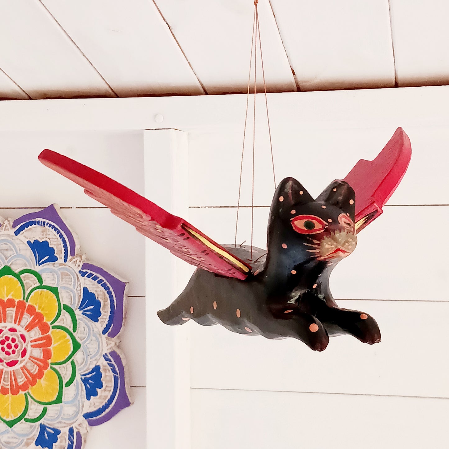 Bring a touch of mystery and magical drama to your home with this striking flying cat mobile, hand carved and painted by skilled artisans in Bali. Featuring a deep black cat with vivid red wings and intricate painted detailing, this unusual hanging decoration makes a bold statement wherever it is displayed.