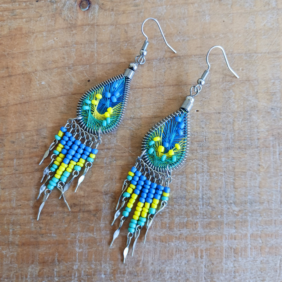 Add a splash of colour to your look with these beautiful handmade Peruvian woven teardrop earrings. Inspired by the vibrant colours and patterns of a peacock feather, each earring features intricate woven detailing complemented by coordinating beads and delicate silver-tone embellishments.