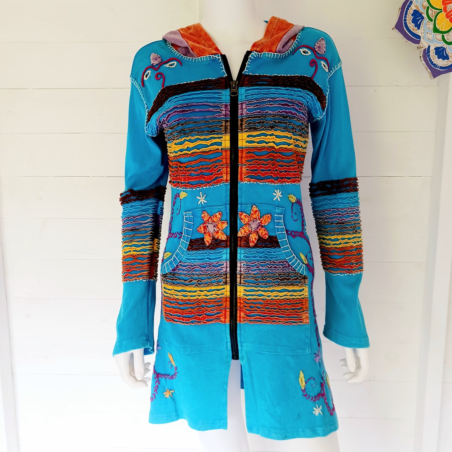 Make a bold statement with this handmade turquoise Pixie Jacket, a striking patchwork coat designed for free spirits and lovers of expressive, bohemian fashion. Crafted in Nepal from soft, stretchy cotton jersey, this longline jacket blends vibrant colours, artistic prints, and intricate detailing into a truly unique outerwear piece.