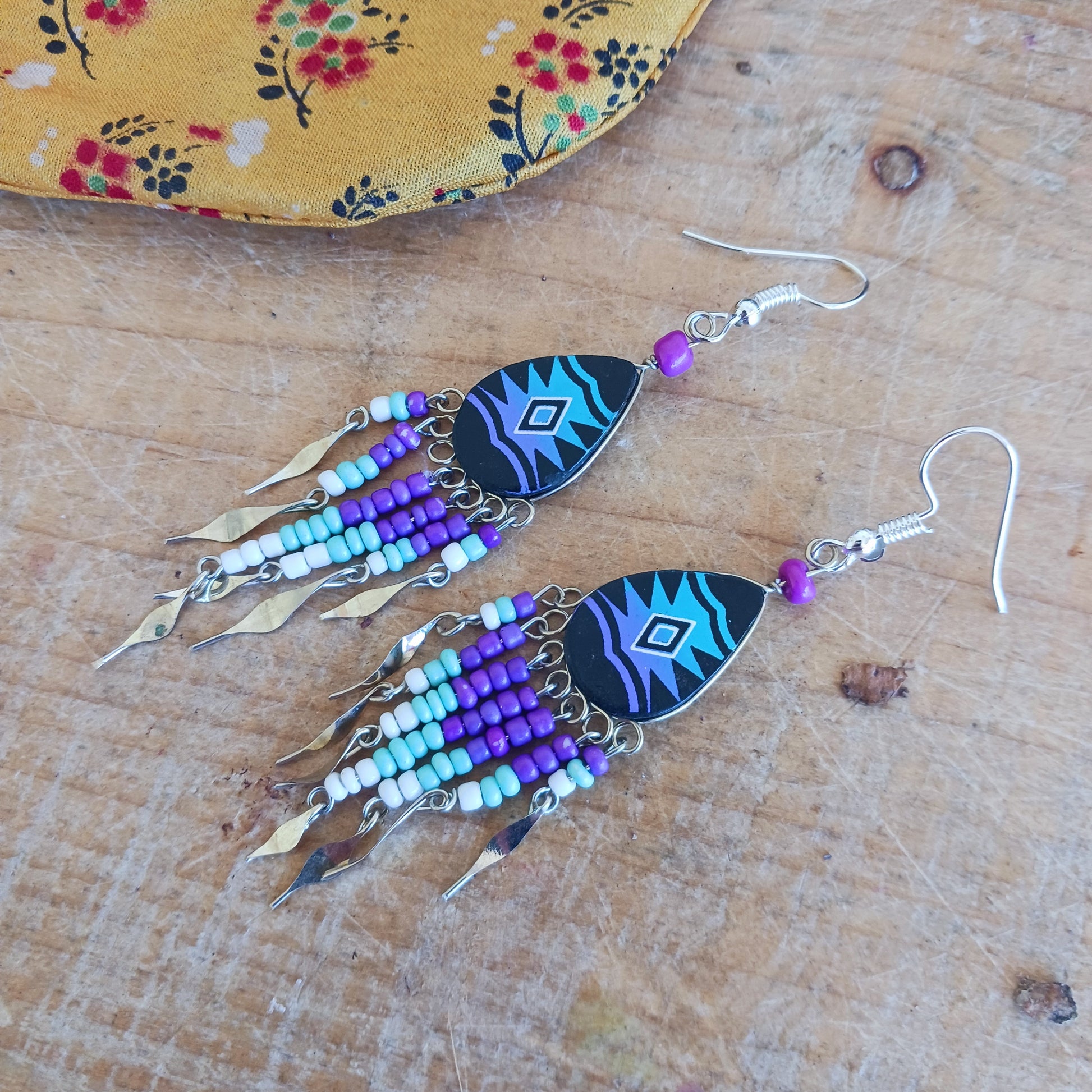 These beautiful and eye-catching earrings are handmade in Peru and feature traditional Incan patterns on the front, the back is coloured black. They are shaped in a teardrop style and are finished with coloured coordinating beads, silver embellishments and silver-plated hooks.