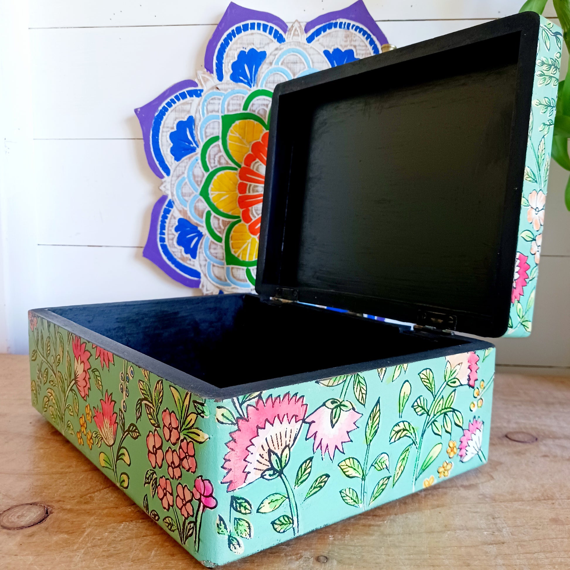 The Saanvi Handcrafted Large Wooden Box is a sustainable gift of beauty, designed to bring charm and practicality to any space. Expertly hand-painted in a bright mixed floral pattern on a pale blue background, this decorative box exudes artisanal elegance. The hinged lid is accented with a small gold-colored knob for a refined touch, while the deep midnight interior offers ample storage for trinkets, jewellery, and cherished keepsakes.