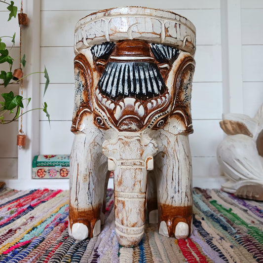 Decorative elephant stool with intricate carvings on a colorful rug.