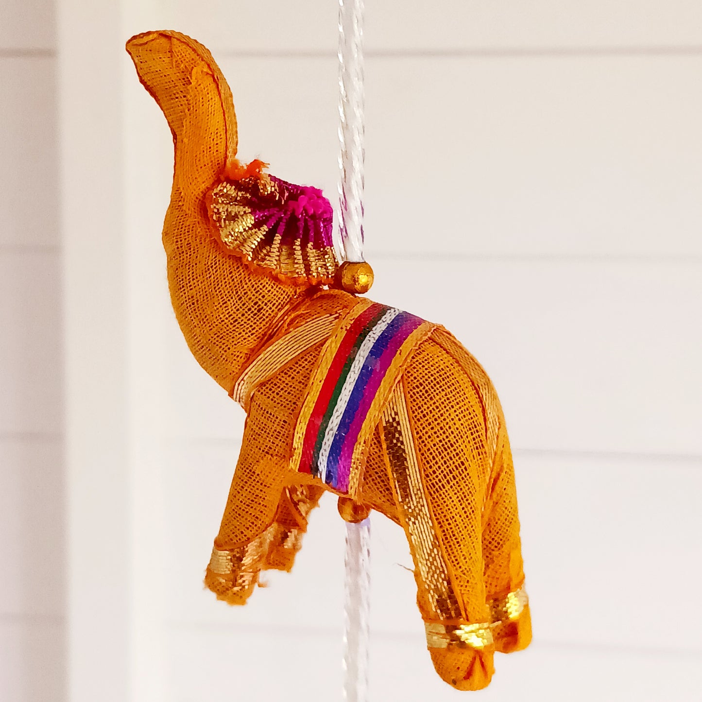 Bring vibrant charm and a touch of global-inspired décor into your home with this beautifully handcrafted stuffed elephant hanging garland. Designed in a traditional tota bell style, this decorative piece features a string of brightly coloured fabric elephants, carefully interspersed with playful beads, mini pom-poms, and delicate jingly bells.