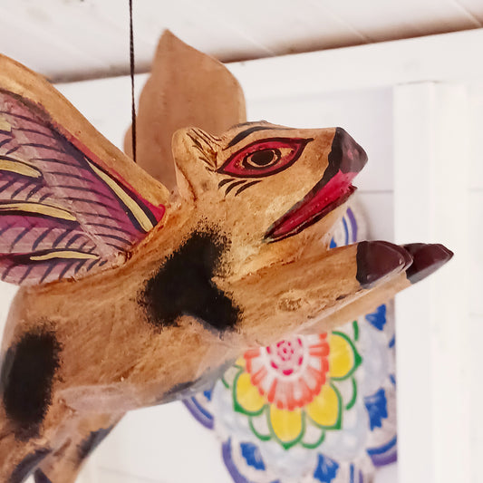 This charming piggy from Bali is categorized as a "Flying Winged Spirit Guardian," also known as a "Cradle Guardian." It is commonly displayed in temples and homes, and hung in elevated areas to repel negative entities. Sometimes, it is purposefully positioned facing downward towards a doorway or window.