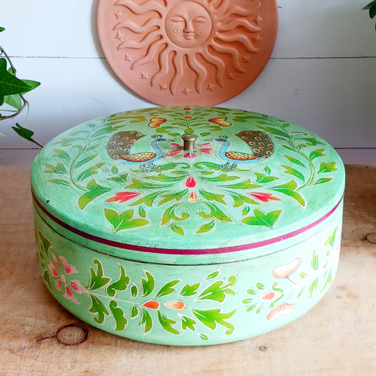Bring a touch of traditional Indian craftsmanship to your home with this beautiful Handmade Indian Wooden Peacock Decorative Box. Expertly crafted from wood and hand-painted by skilled artisans, this charming round storage box features an elegant peacock design on the pull-off lid, symbolizing beauty, grace, and prosperity.
