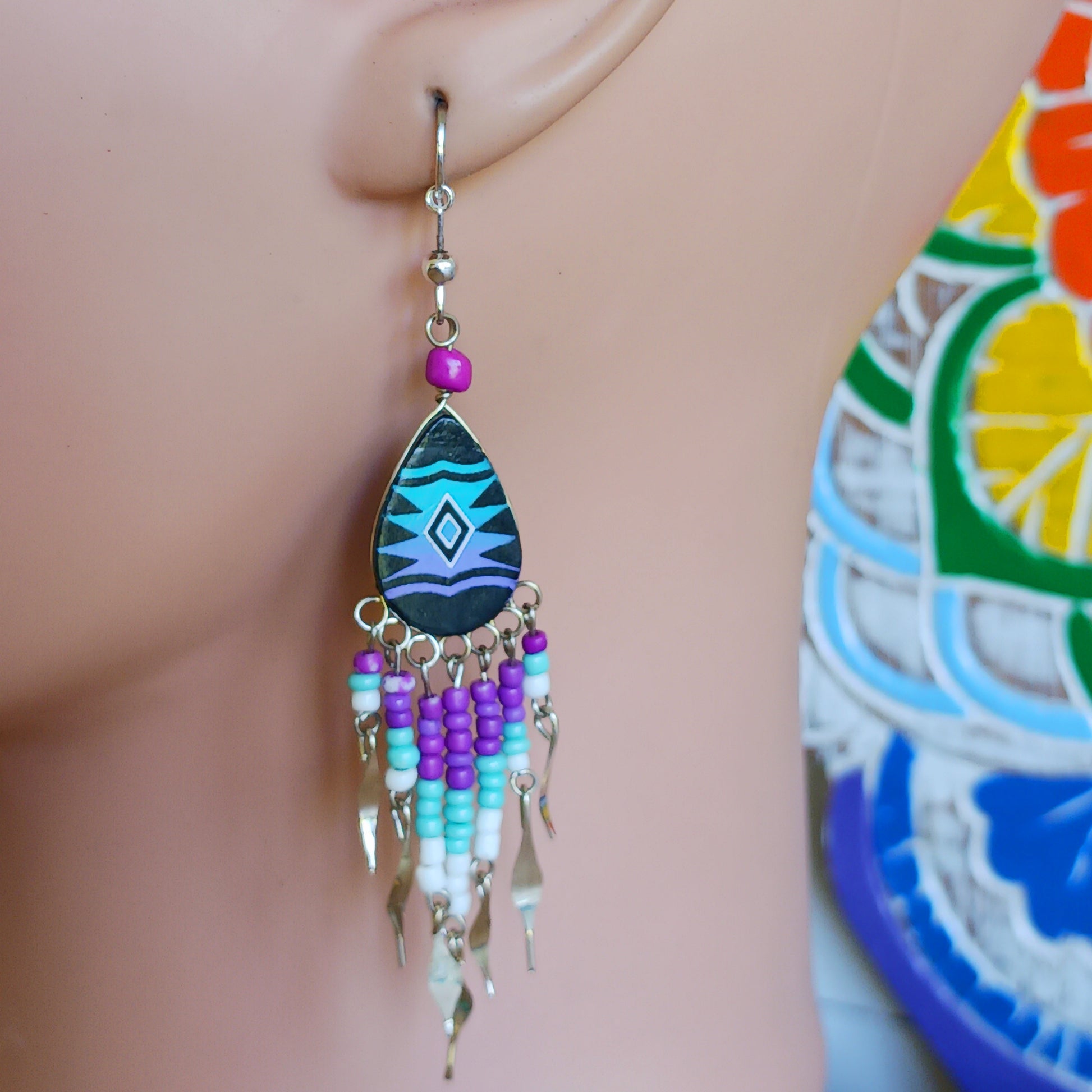 These beautiful and eye-catching earrings are handmade in Peru and feature traditional Incan patterns on the front, the back is coloured black. They are shaped in a teardrop style and are finished with coloured coordinating beads, silver embellishments and silver-plated hooks.