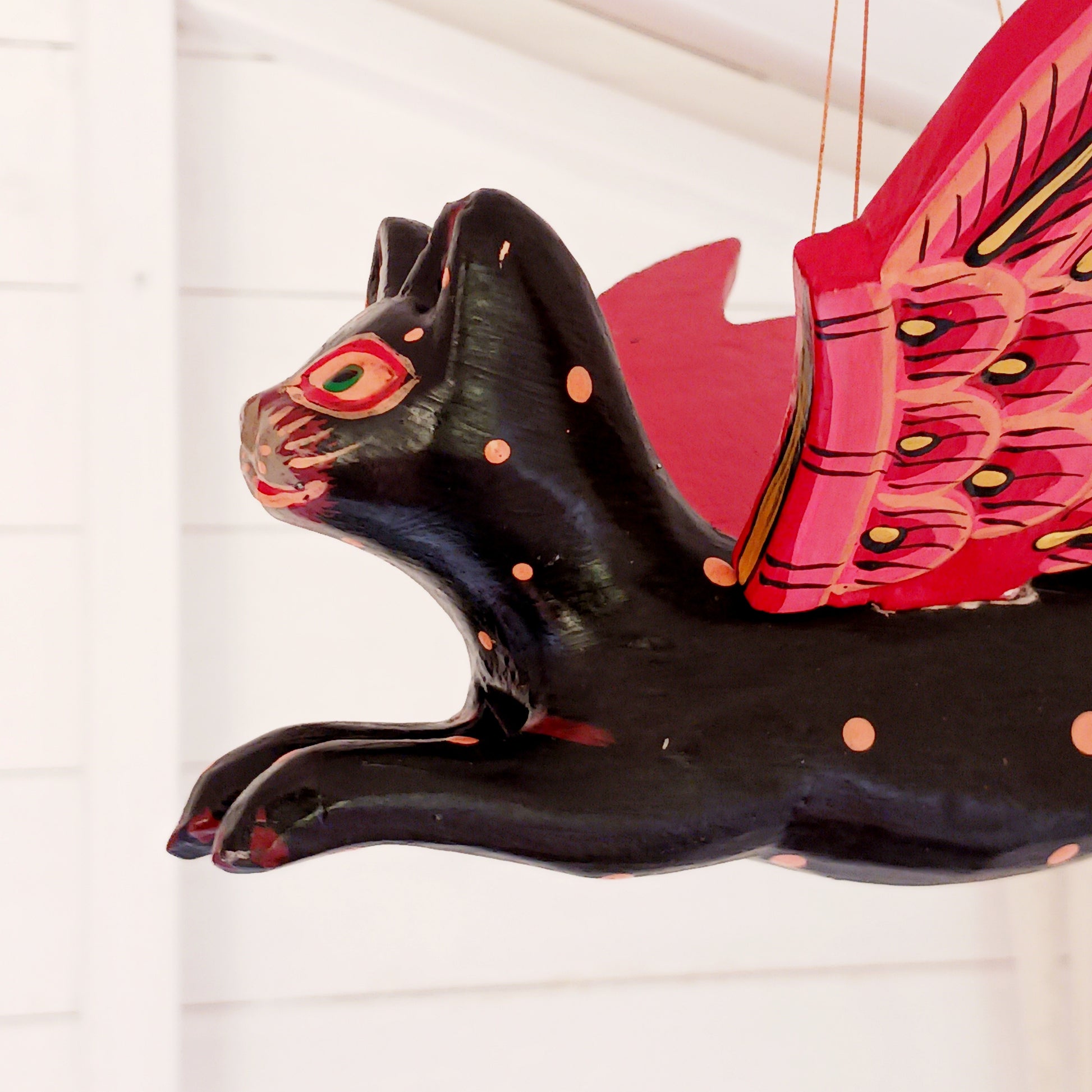 Bring a touch of mystery and magical drama to your home with this striking flying cat mobile, hand carved and painted by skilled artisans in Bali. Featuring a deep black cat with vivid red wings and intricate painted detailing, this unusual hanging decoration makes a bold statement wherever it is displayed.