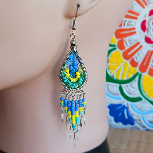 Add a splash of colour to your look with these beautiful handmade Peruvian woven teardrop earrings. Inspired by the vibrant colours and patterns of a peacock feather, each earring features intricate woven detailing complemented by coordinating beads and delicate silver-tone embellishments.