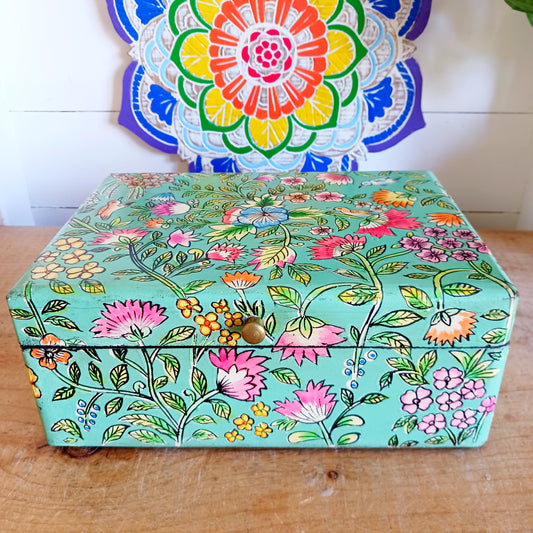 The Saanvi Handcrafted Large Wooden Box is a sustainable gift of beauty, designed to bring charm and practicality to any space. Expertly hand-painted in a bright mixed floral pattern on a pale blue background, this decorative box exudes artisanal elegance. The hinged lid is accented with a small gold-colored knob for a refined touch, while the deep midnight interior offers ample storage for trinkets, jewellery, and cherished keepsakes.