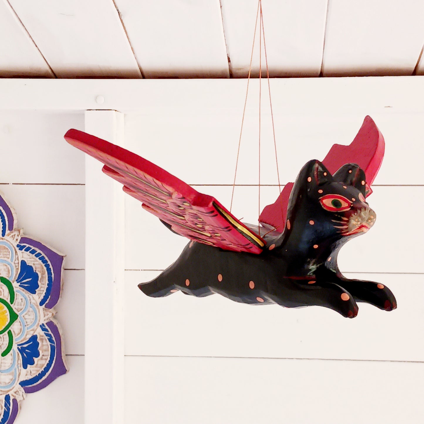 Bring a touch of mystery and magical drama to your home with this striking flying cat mobile, hand carved and painted by skilled artisans in Bali. Featuring a deep black cat with vivid red wings and intricate painted detailing, this unusual hanging decoration makes a bold statement wherever it is displayed.