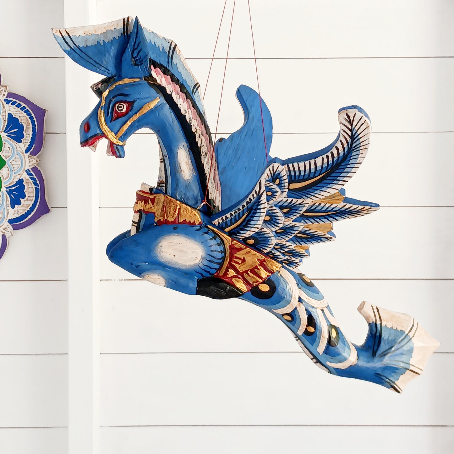Bring a touch of fantasy to your home with this beautifully handcrafted winged seahorse hanging mobile. Hand-painted in vivid cobalt blue, this enchanting wooden seahorse features intricate painted scales, feather-like detailing and traditional Balinese-inspired decoration.