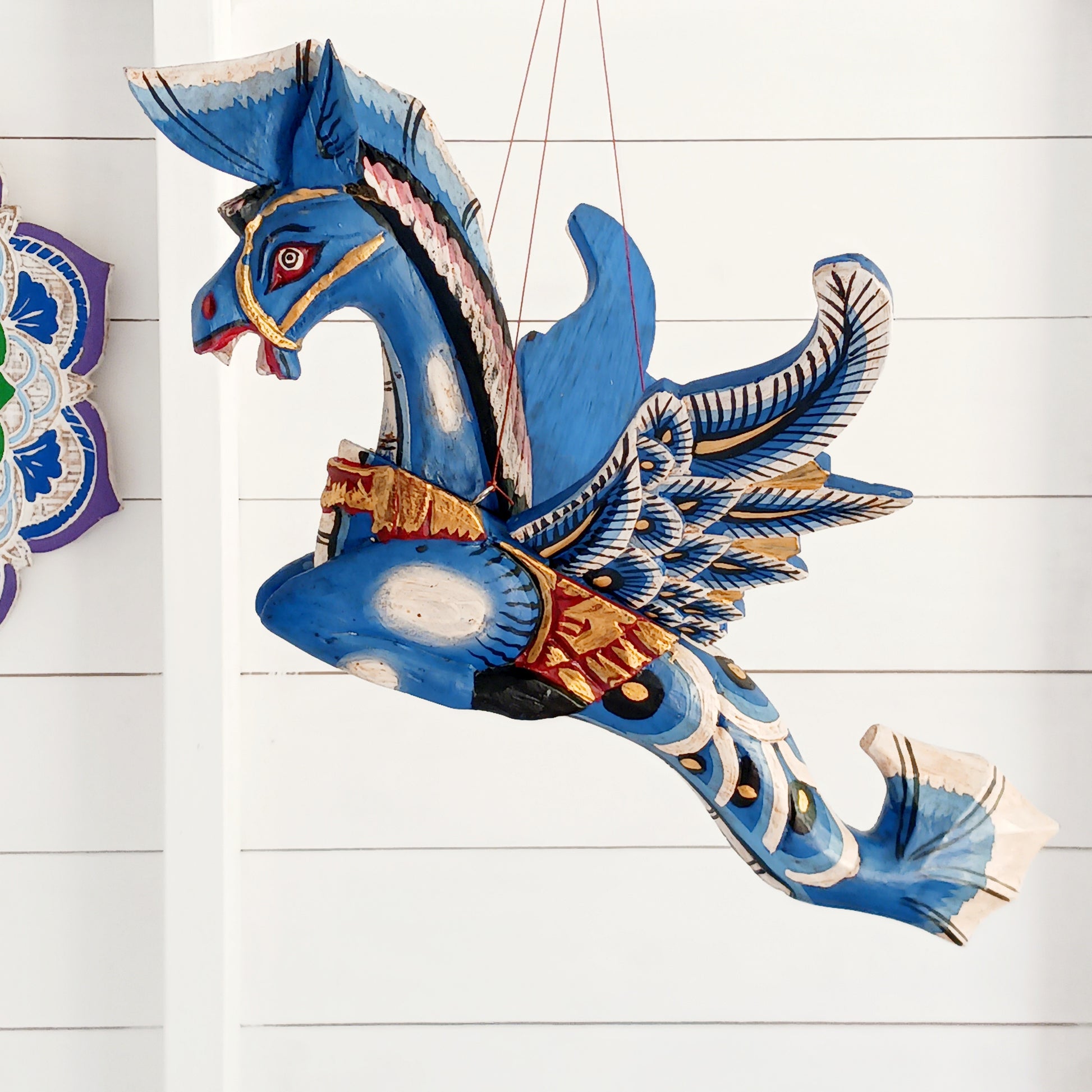 Bring a touch of fantasy to your home with this beautifully handcrafted winged seahorse hanging mobile. Hand-painted in vivid cobalt blue, this enchanting wooden seahorse features intricate painted scales, feather-like detailing and traditional Balinese-inspired decoration.