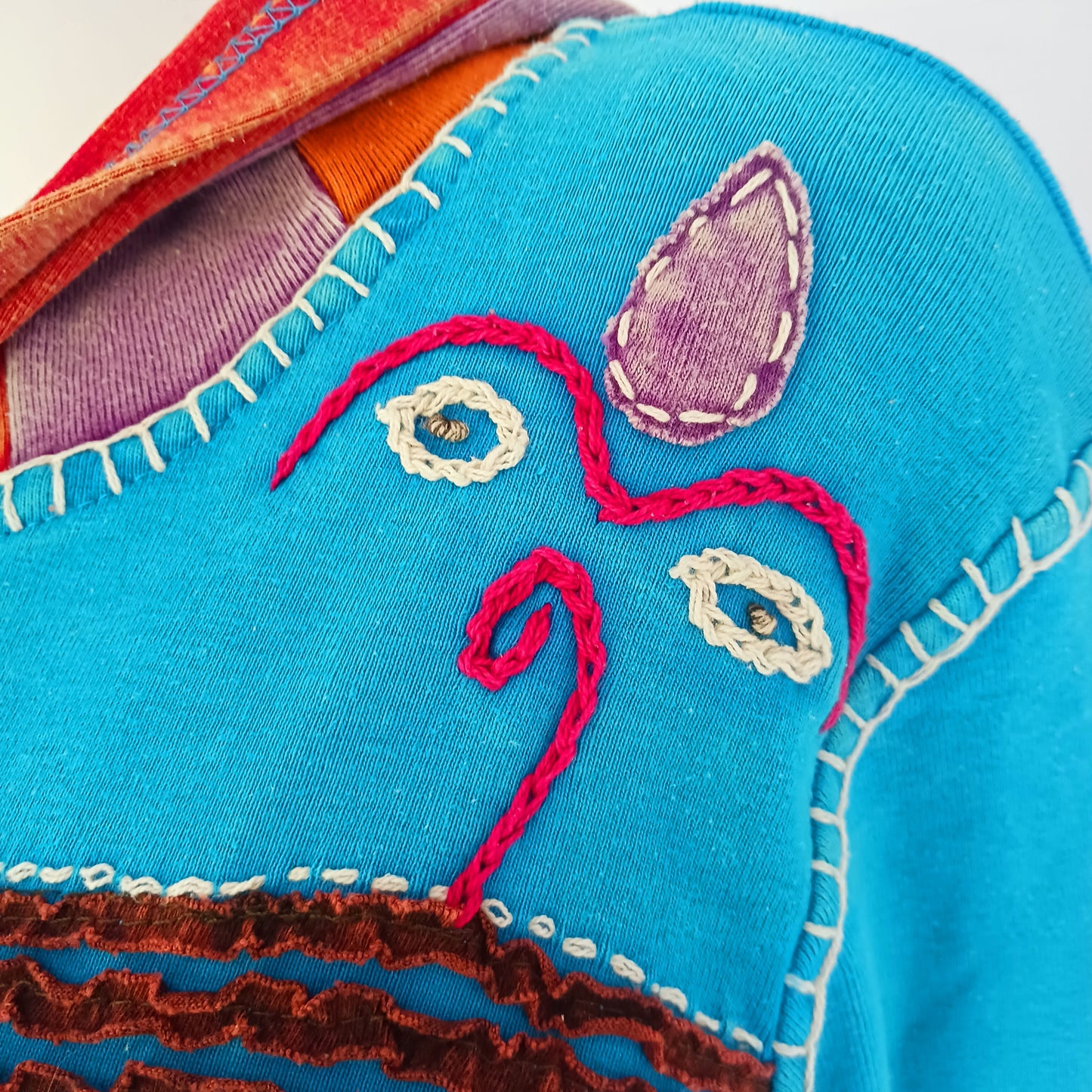 Make a bold statement with this handmade turquoise Pixie Jacket, a striking patchwork coat designed for free spirits and lovers of expressive, bohemian fashion. Crafted in Nepal from soft, stretchy cotton jersey, this longline jacket blends vibrant colours, artistic prints, and intricate detailing into a truly unique outerwear piece.