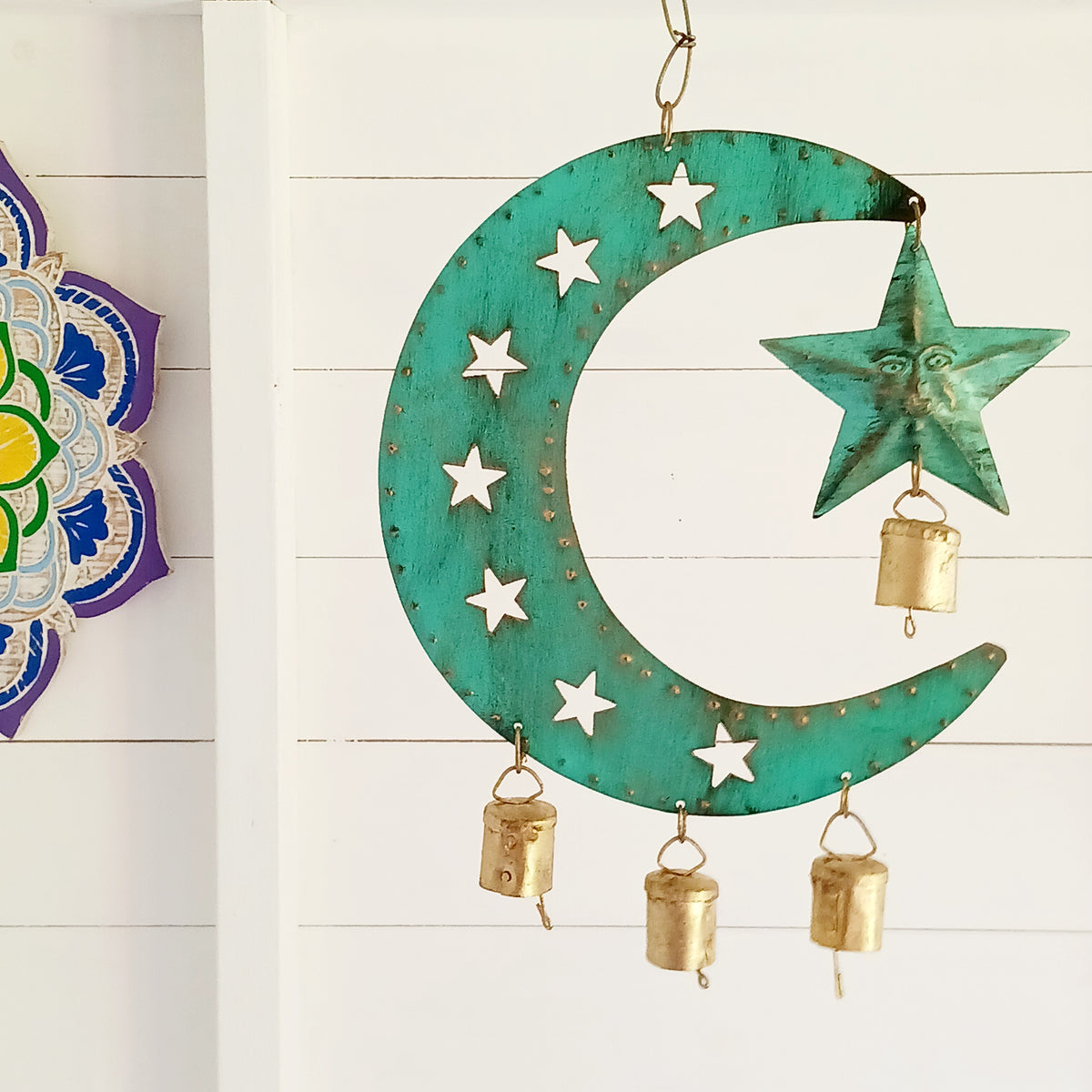 Bring a touch of celestial charm to your home with this rustic crescent moon wind chime, beautifully finished in an aged verdigris green. Handmade by skilled artisans in India, this decorative iron wall hanging features pierced star detailing, a hanging star charm and traditional Indian brass bells.