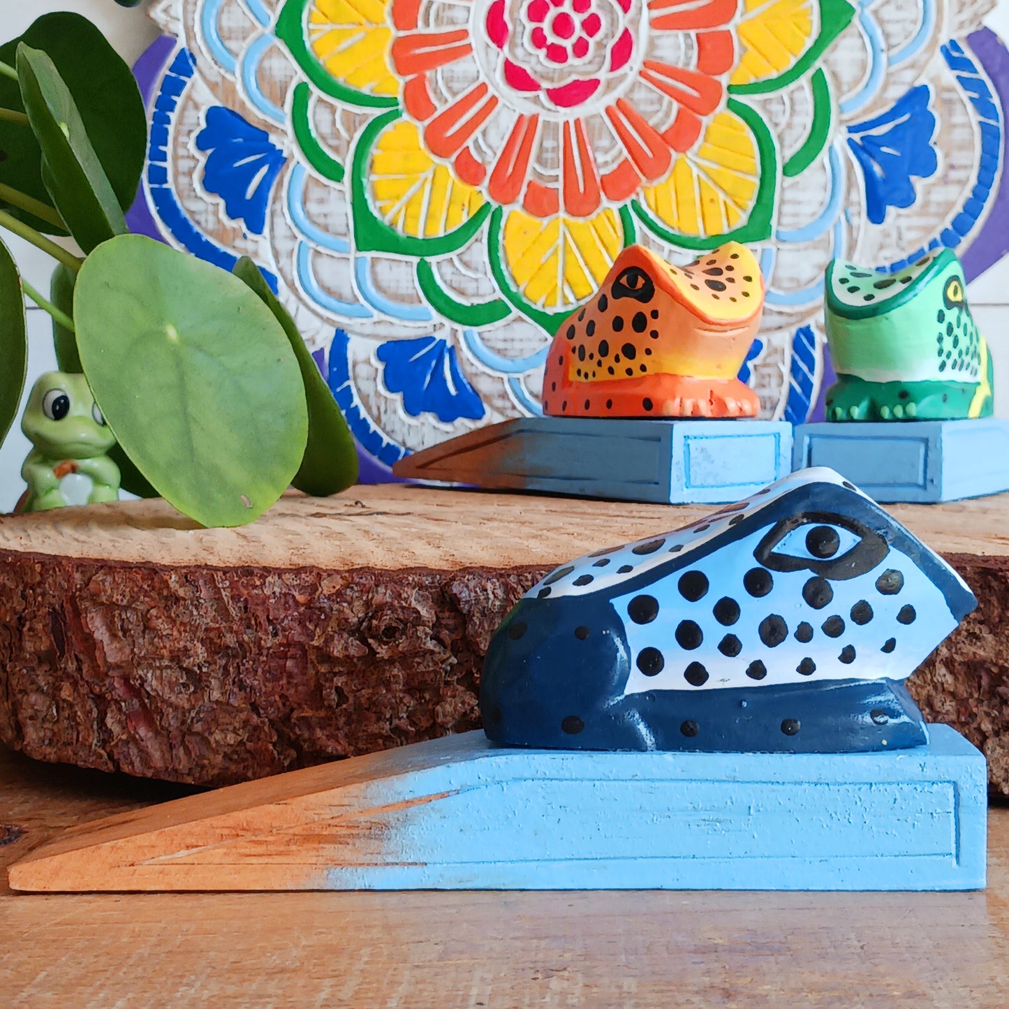 Bring charm and character into your home with this decorative wooden door stopper, featuring a turquoise base and a playful, hand-painted dotty frog design in vibrant blue, green, and orange. Perfect for propping open doors in style, this quirky wedge door stop is both practical and fun.