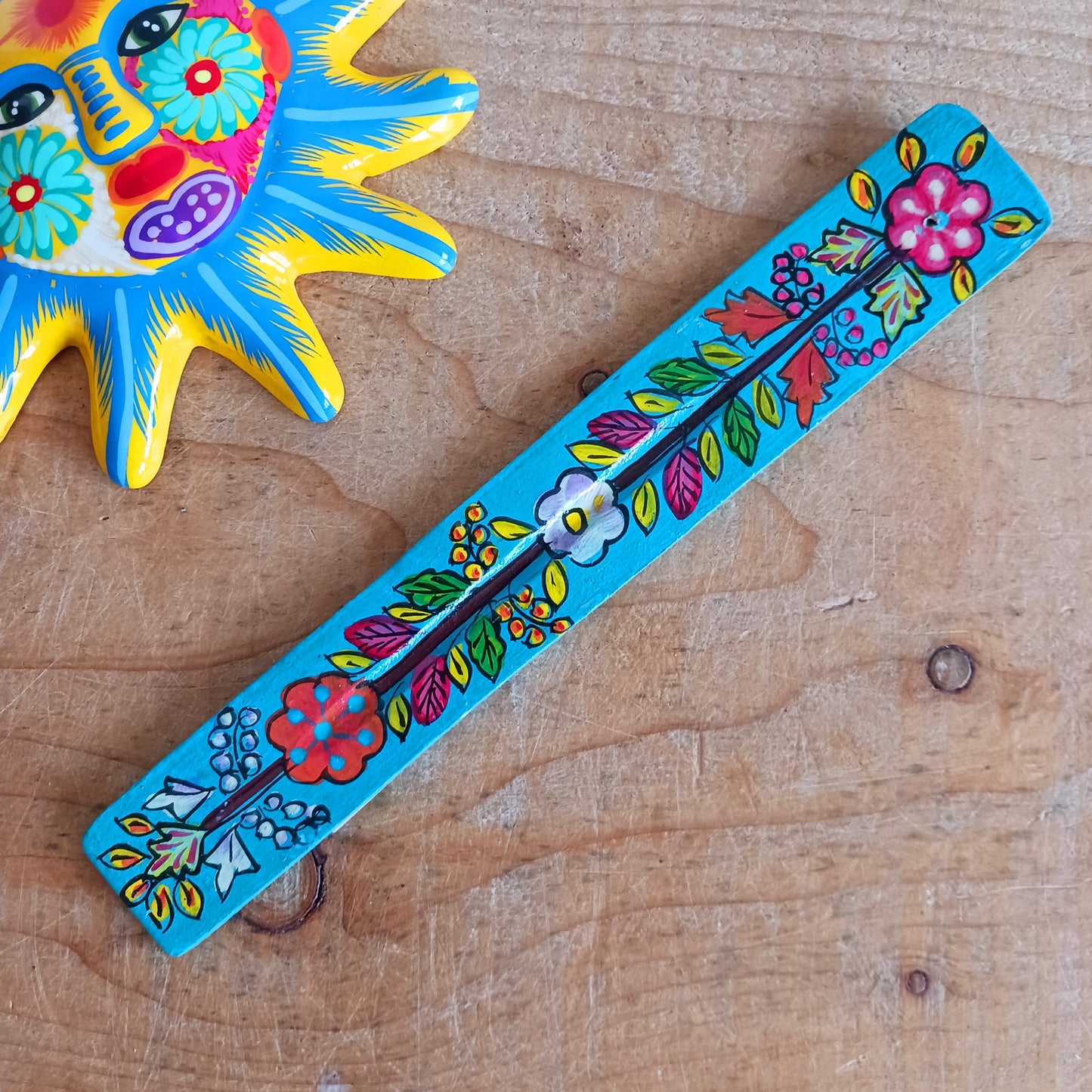 This wooden incense stick holder is hand-painted with decorative floral designs. Sourced from India in a fairtrade manner, this product serves as both an aesthetically pleasing decoration and an effective ash catcher for any home.