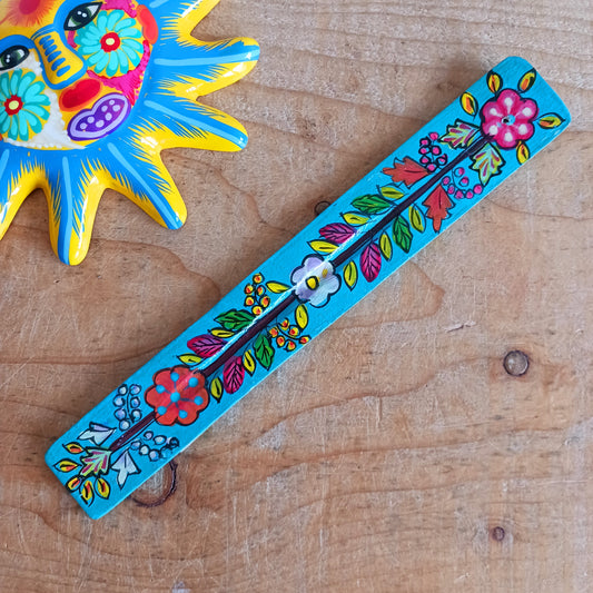 This wooden incense stick holder is hand-painted with decorative floral designs. Sourced from India in a fairtrade manner, this product serves as both an aesthetically pleasing decoration and an effective ash catcher for any home.