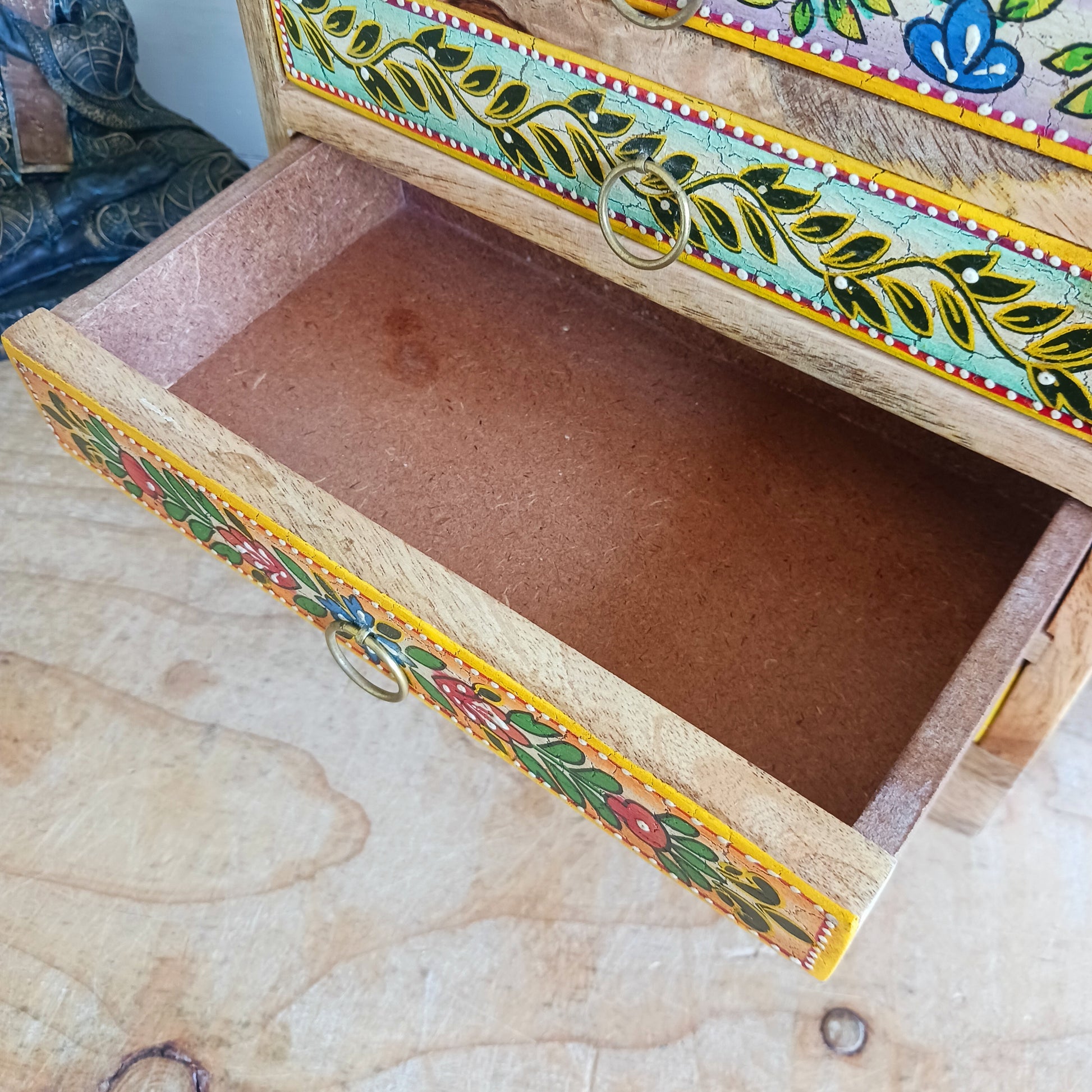 Add charm and functionality to your space with the Zaha Hand-Painted 6 Drawer Mango Wood Chest. Standing gracefully on low corner feet, this artisan-crafted piece features a vibrant blend of hand-painted leafy vines, amber-toned framing, and highlighted beading. Each drawer is uniquely designed and fitted with elegant gold-toned ring pull handles, offering a burst of colour and creativity.