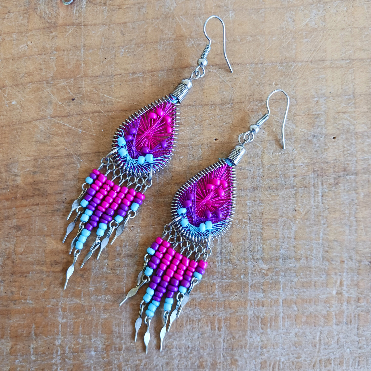 Add a splash of colour to your look with these beautiful handmade Peruvian woven teardrop earrings. Inspired by the vibrant colours and patterns of a peacock feather, each earring features intricate woven detailing complemented by coordinating beads and delicate silver-tone embellishments.